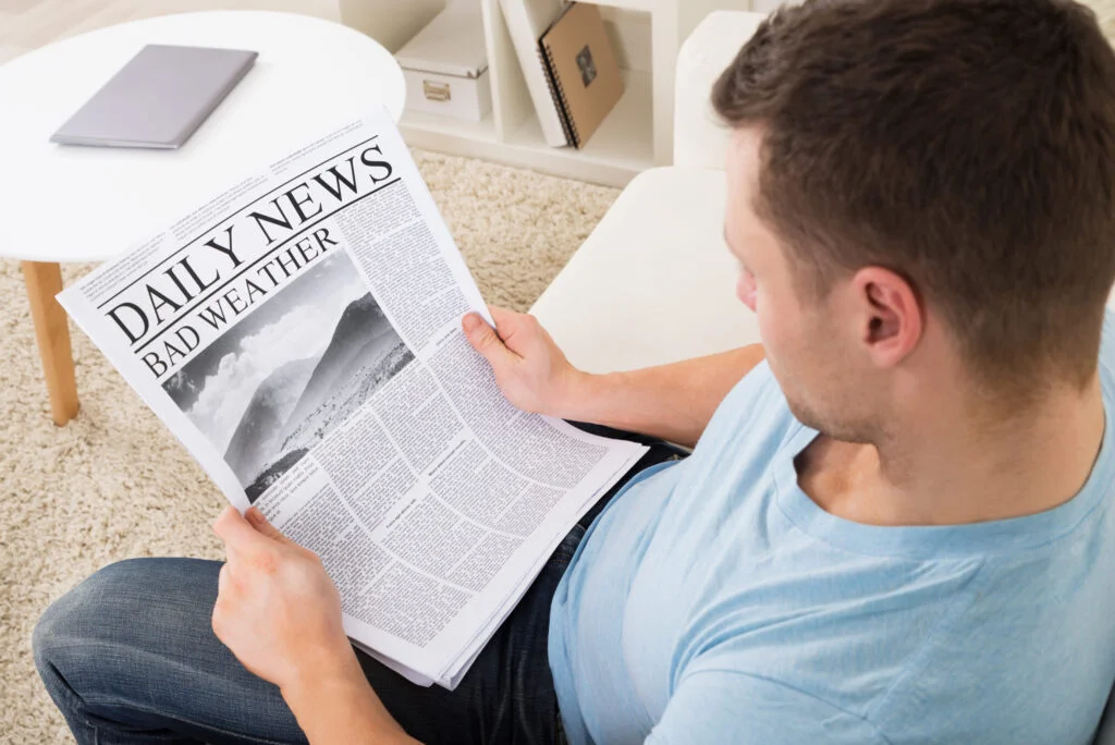 Man Reading Weather News On Newspaper At Home