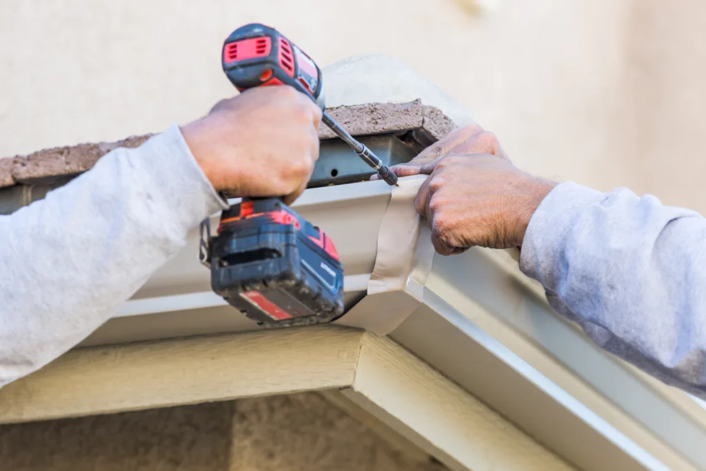 How to Install Rain Gutters - Workers Attaching Aluminum Rain Gutter to Fascia of House