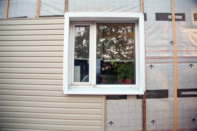 Wall covering of the frame house with panels of vinyl siding of gray color. Decorating the house with siding